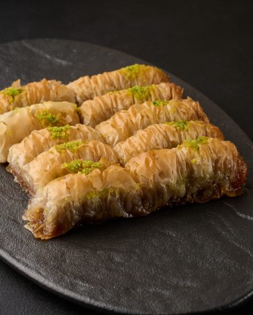 Pieces of baked baklava in honey and sprinkled with pistachios o Pieces of baked baklava in honey and sprinkled with pistachios on a black board